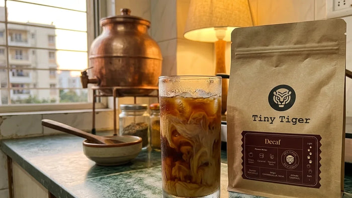 Decaf cold brew over ice with milk, beside a bag of Tiny Tiger Decaffeinated Toasted Almond
