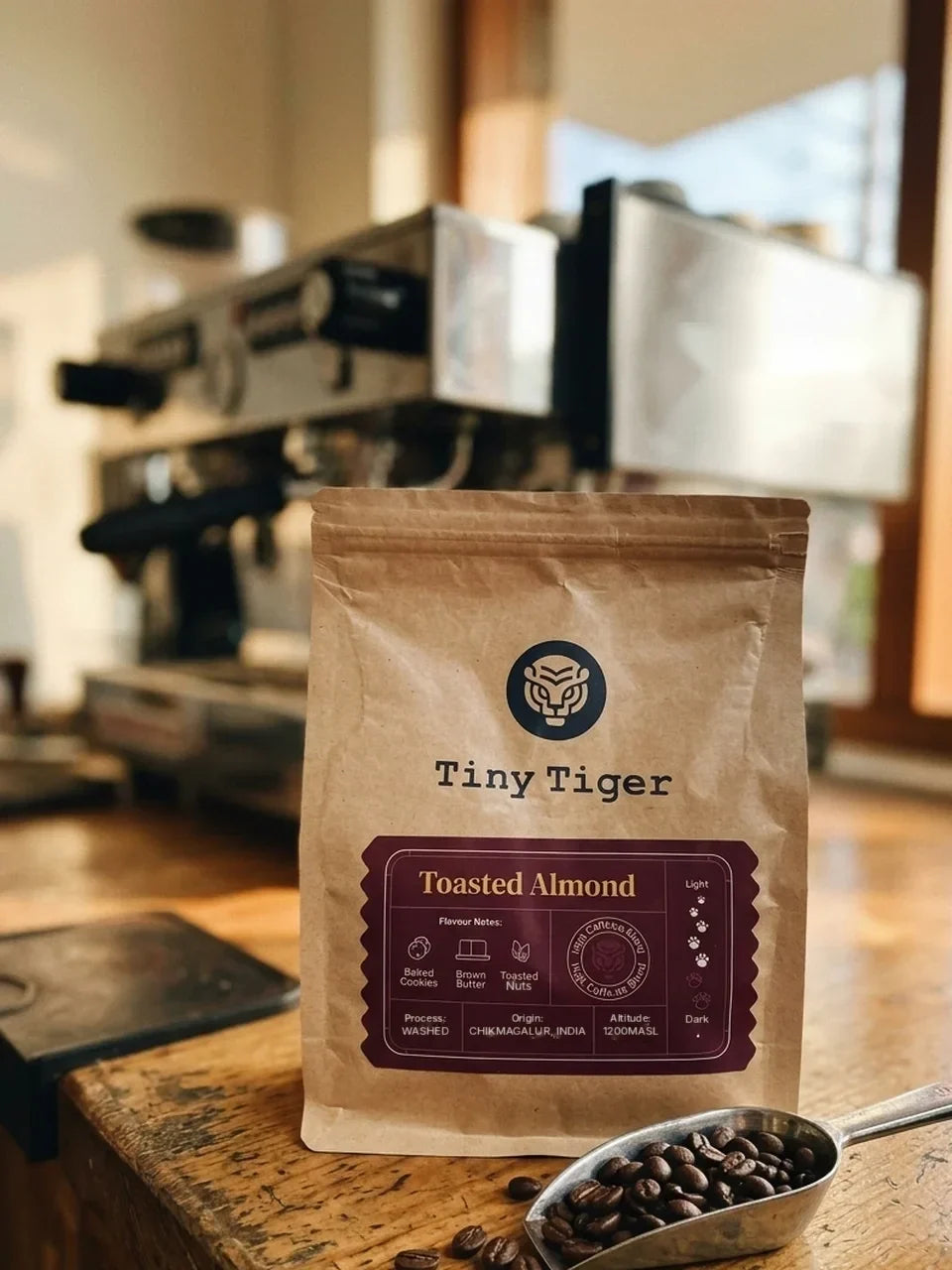 A Tiny Tiger Toasted Almond coffee pouch on a café counter beside roasted coffee beans