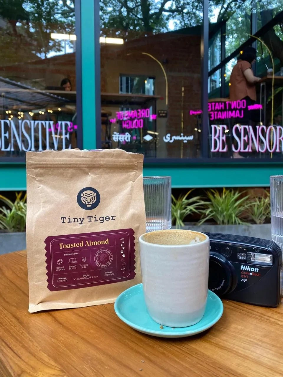 Tiny Tiger Toasted Almond coffee bag beside a cappuccino at a café
